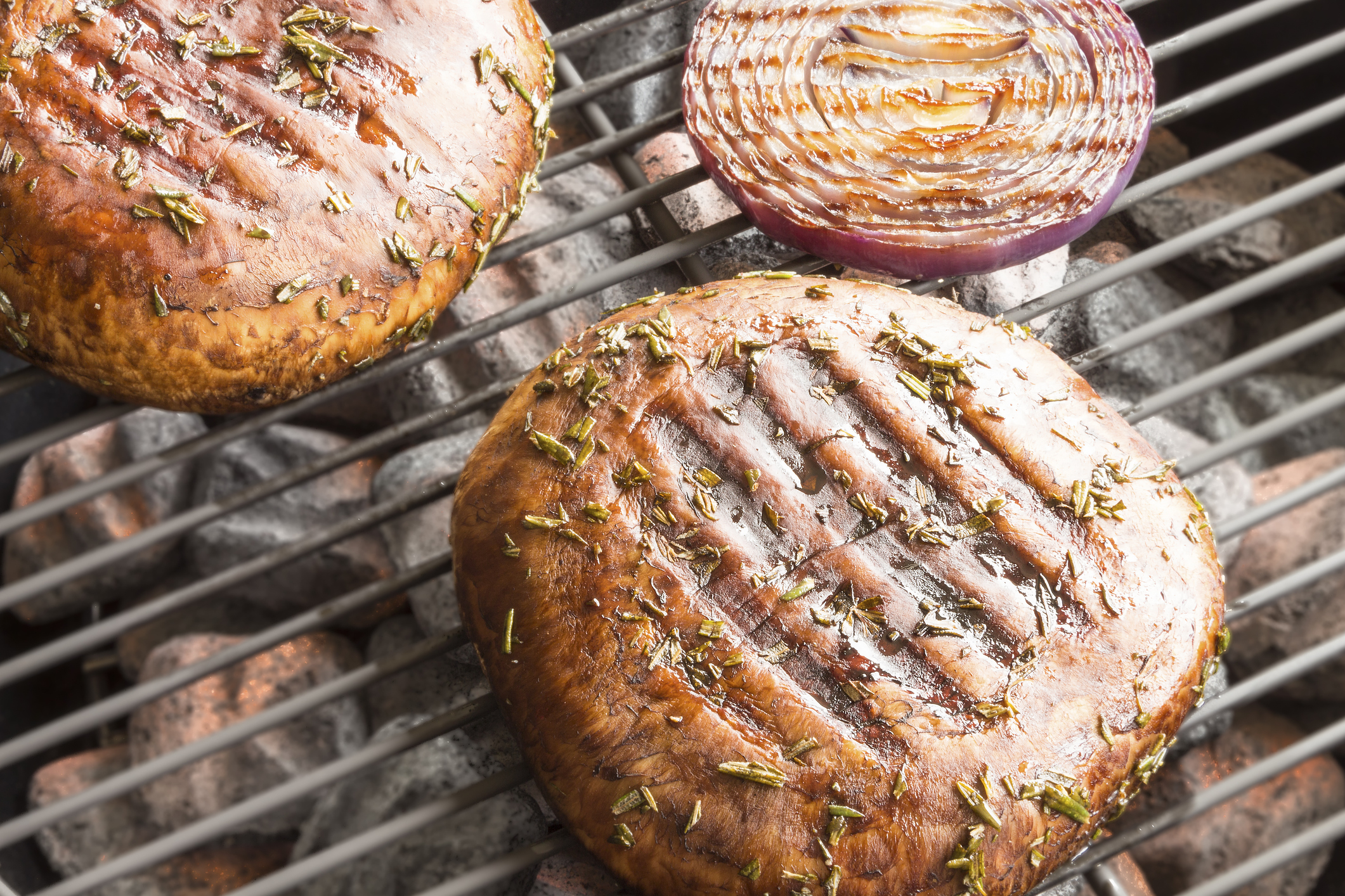 Two portobello mushrooms marinated and grilling with purple onion