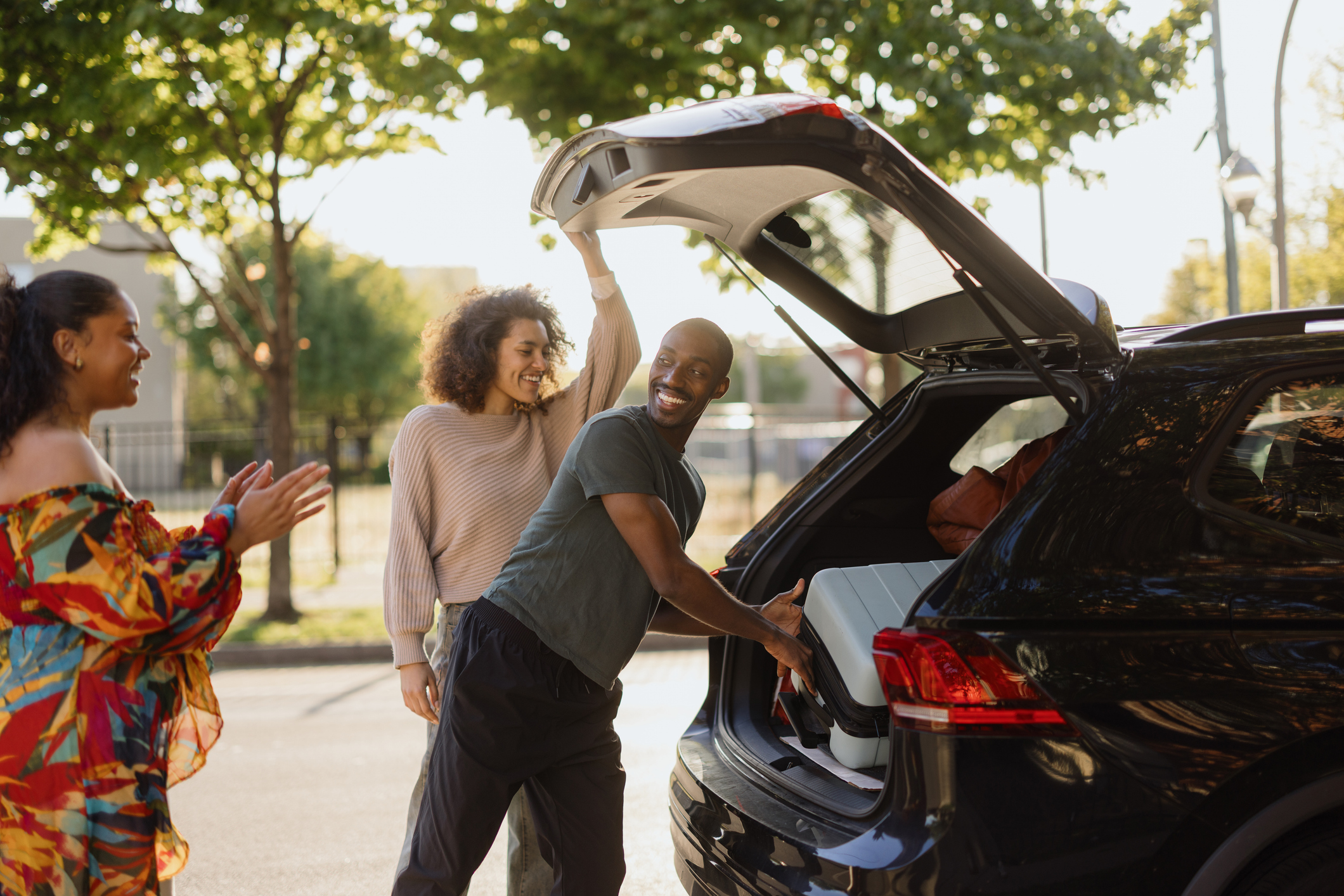Happy friends packing luggage into car for road trip